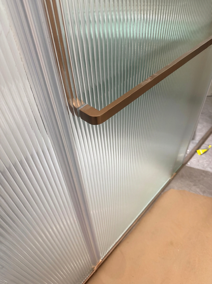 Reeded glass partition detail with brushed bronze framing and handle
